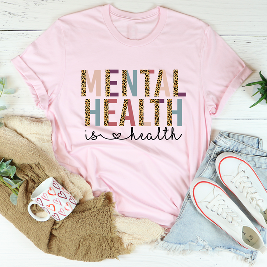 Pink t-shirt with 'Mental Health is Health' text on a white surface with accessories.