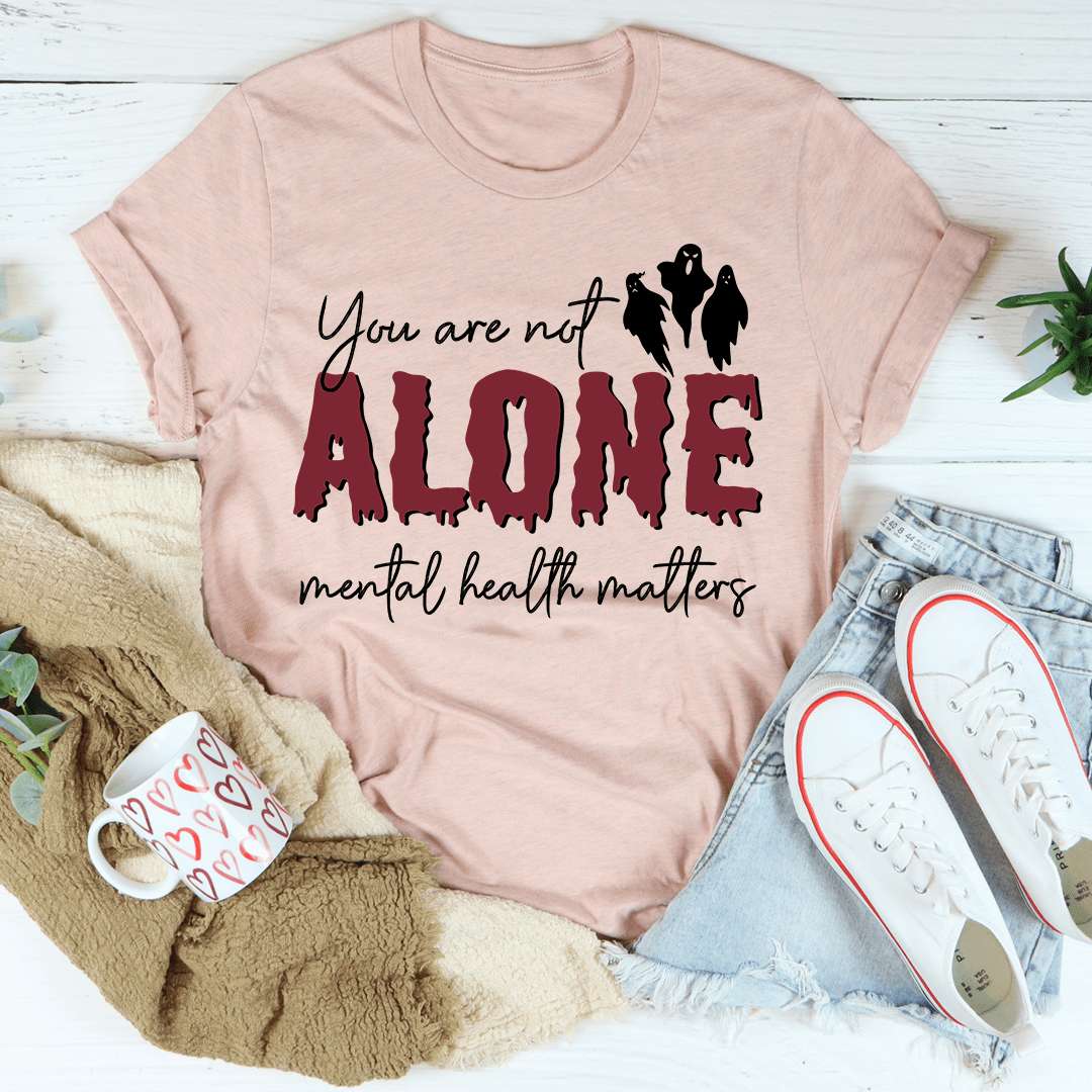 Pink t-shirt with 'You are not alone, mental health matters' text on a white surface with accessories.