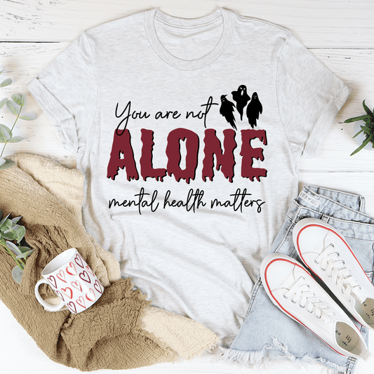 White t-shirt with 'You are not alone' mental health message on a white background with casual items.