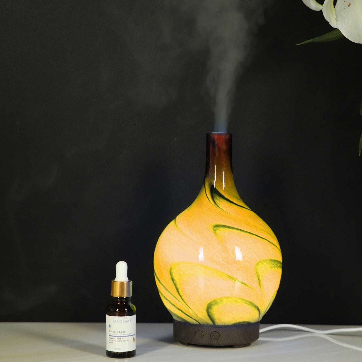 Decorative diffuser with steam emitting, next to a small bottle on a dark background